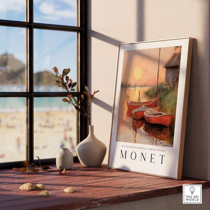 Claude Monet art print of red boats at sunset displayed on a windowsill with a beach view in the background.
