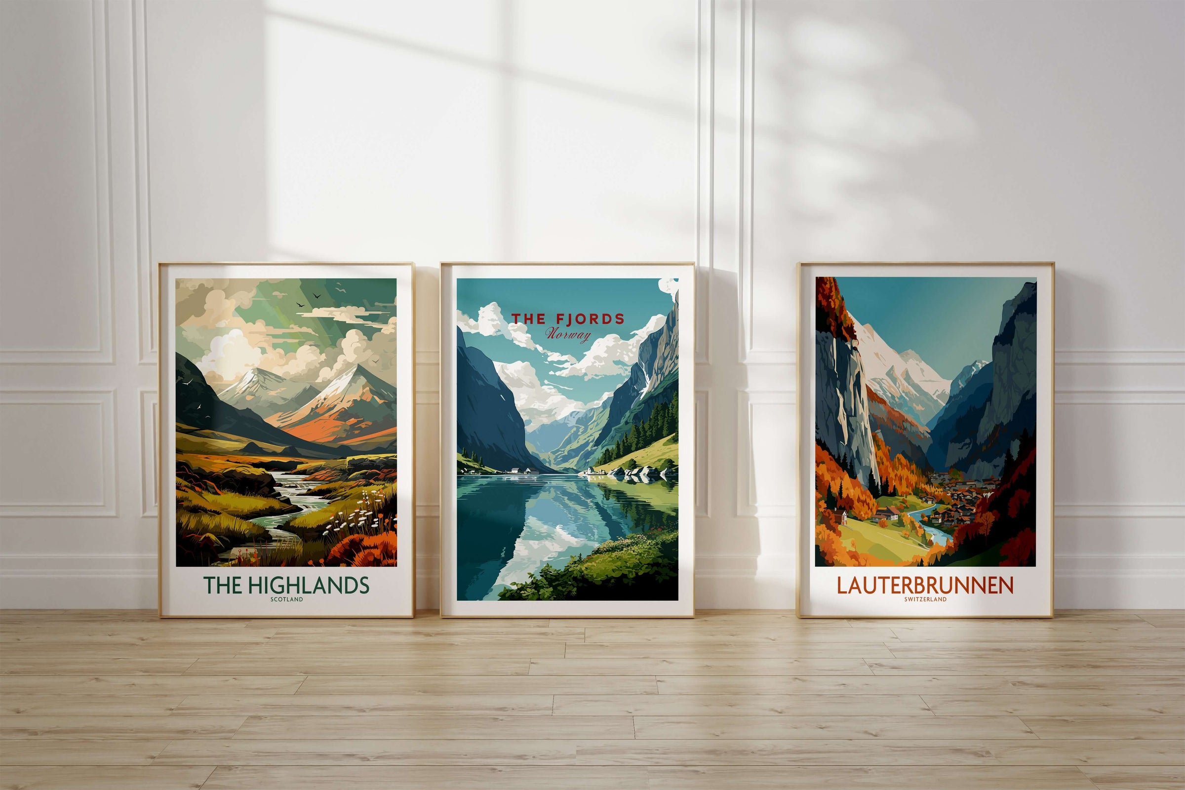 A set of three framed travel poster prints in natural wood frames resting on the floor. Featuring the locations of The Highlands in Scotland, The Fjords in Norway and Lauterbrunnen in Switzerland. 