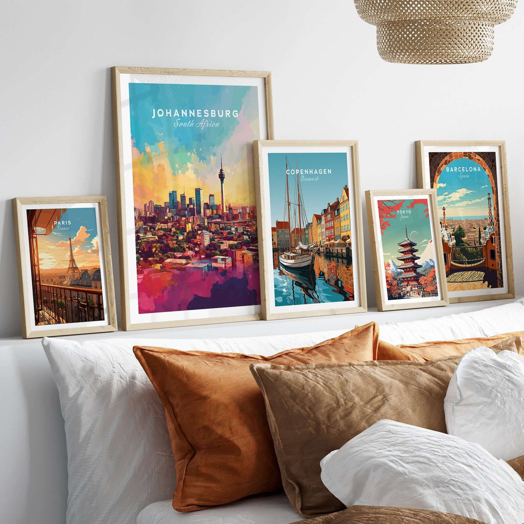 Framed art prints of Johannesburg skyline, Copenhagen, and Barcelona on a stylish bed with cushions.