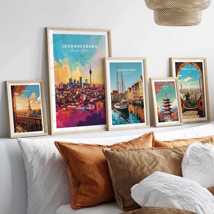 Framed art prints of Johannesburg skyline, Copenhagen, and Barcelona on a stylish bed with cushions.