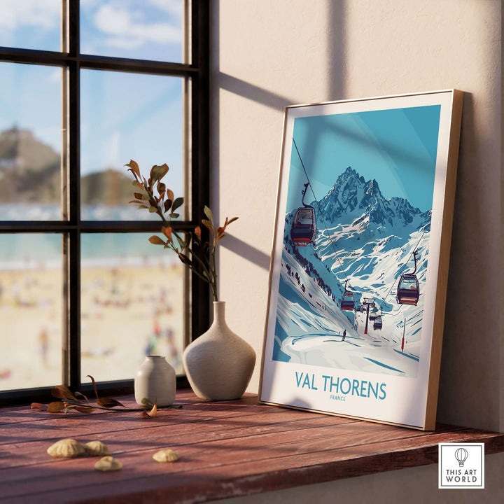 Val Thorens ski resort poster displayed on a wooden table near a sunny window, showcasing stunning mountain scenery.