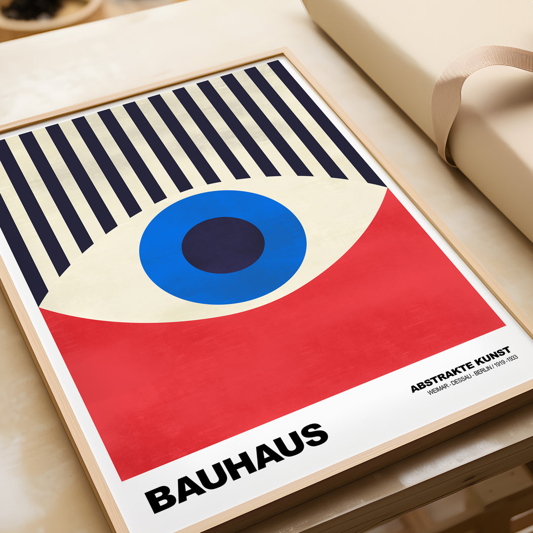 Bauhaus exhibition print featuring abstract eye art in geometric red and blue design, framed on a table.