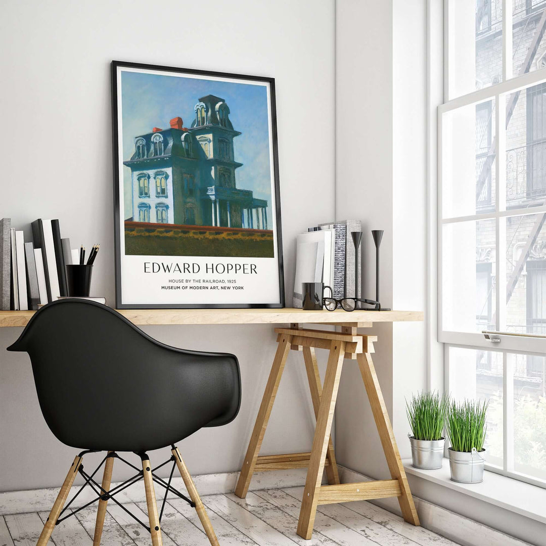 Edward Hopper House by the Railroad art print poster framed in modern office space with desk and chair.