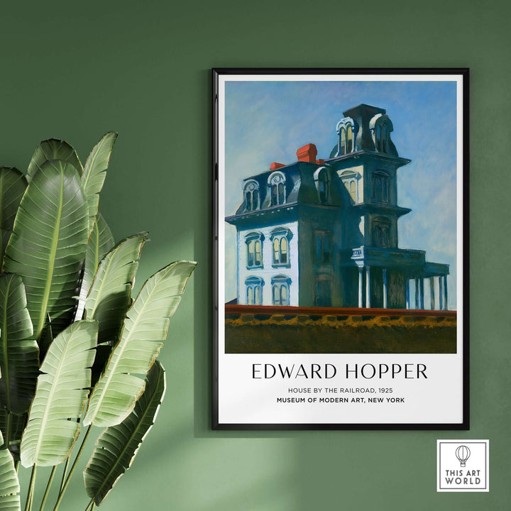 Edward Hopper's House by the Railroad 1925 art print poster framed against a green wall with plants.
