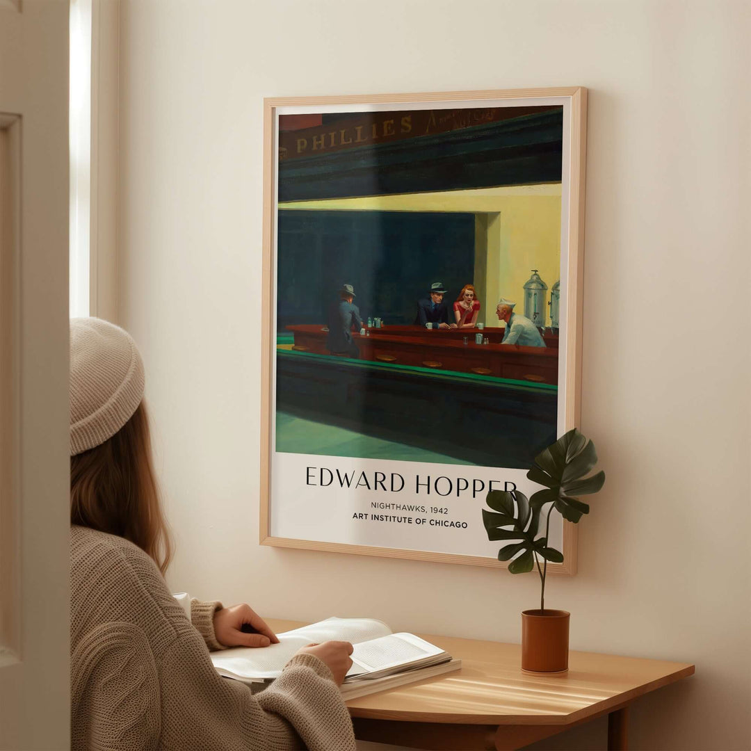 Person reading near Edward Hopper Nighthawks 1942 art print at home, showcasing iconic diner scene.