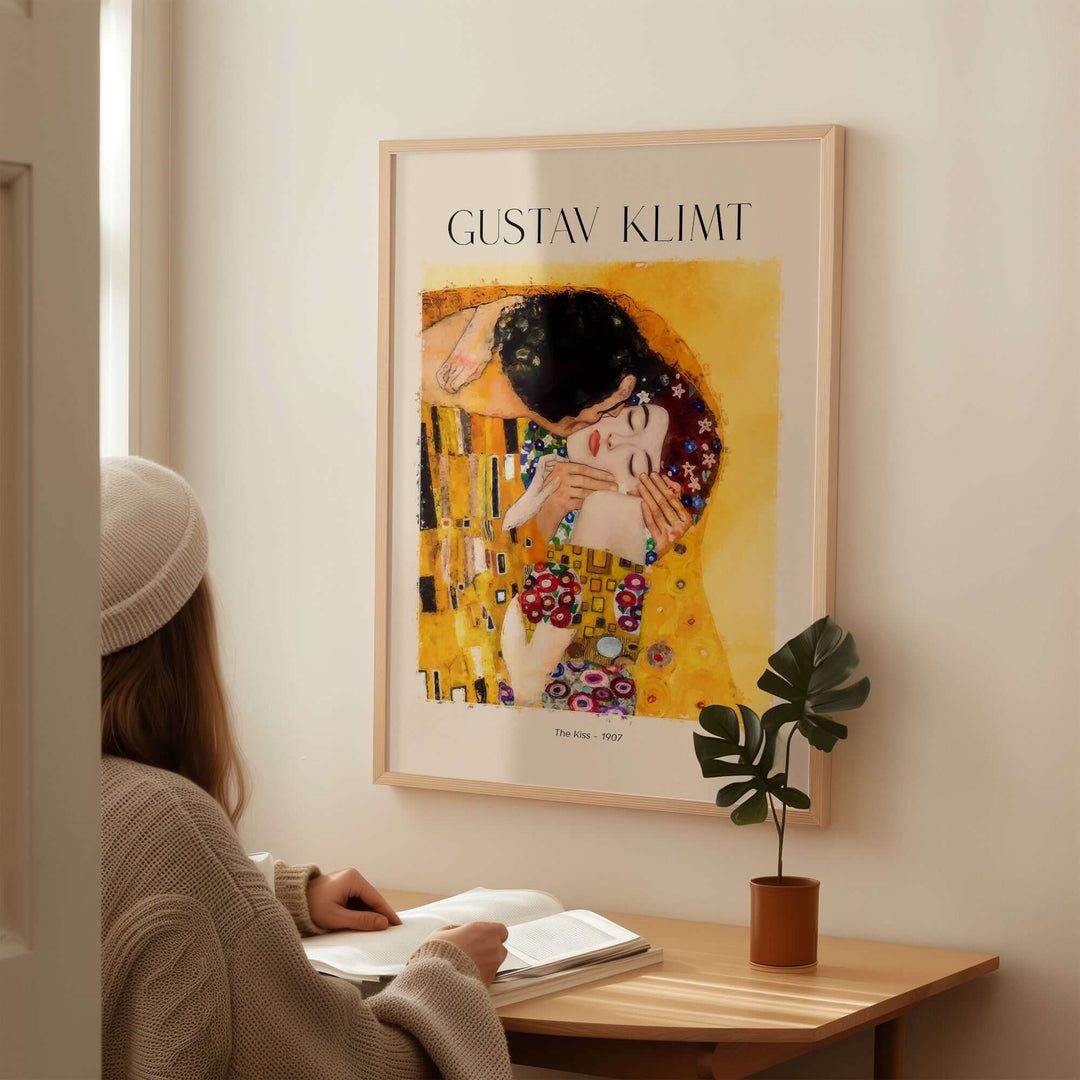 Gustav Klimt art print 'The Kiss' 1907 displayed in a cozy interior setting with a person reading.