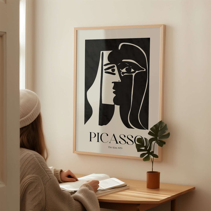 Woman sitting at a desk, admiring Picasso's 'The Kiss' 1979 black and white abstract wall art print.