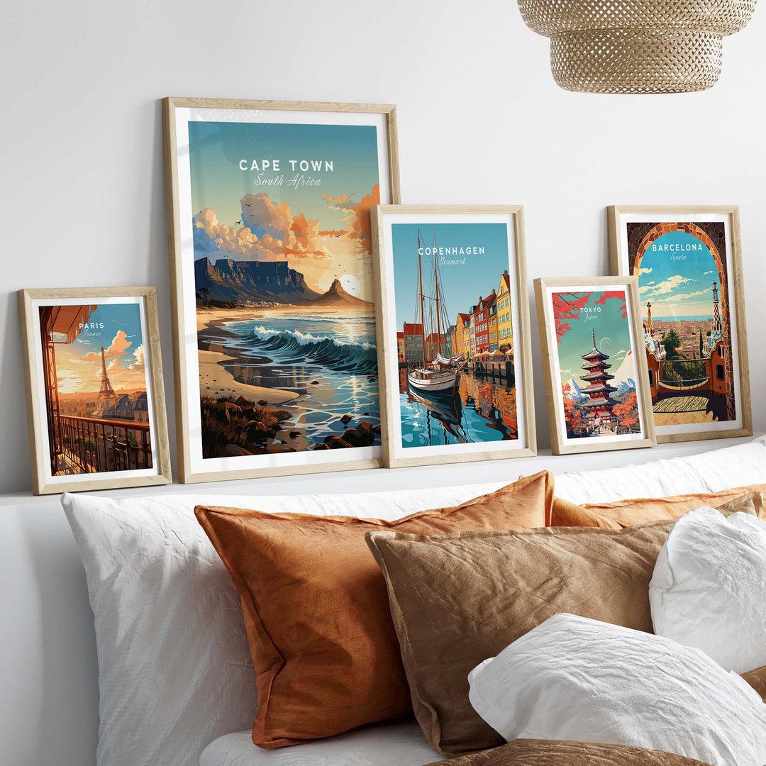 Framed travel posters of Cape Town, Copenhagen, and Barcelona displayed on a cozy bed with decorative pillows.