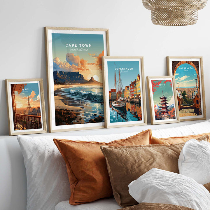 Framed travel posters of Cape Town, Copenhagen, and Barcelona displayed on a cozy bed with decorative pillows.