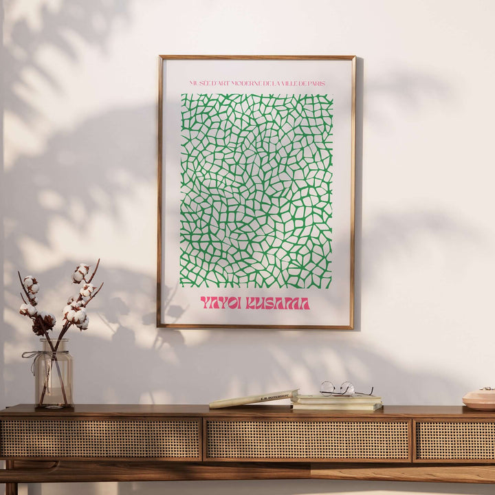 Yayoi Kusama green net pattern art print framed on wall above a wooden console table with decor.
