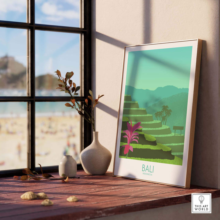 Bali Print artwork on a wooden table with a view of the beach, showcasing vibrant green terraces and tropical plants.