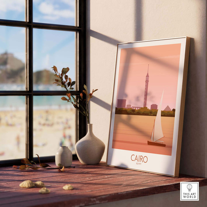 Cairo travel poster print displayed on a wooden table, featuring the Nile River and iconic buildings, with a beach view in the background.