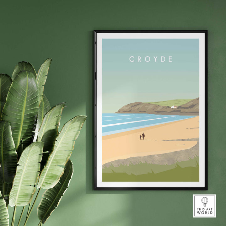 Croyde Poster Print Wall Art featuring a beach scene, framed on a green wall with plants, perfect for home decor.