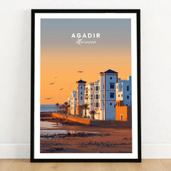 Agadir Travel Poster – Morocco Beach Print in a black wooden frame leaning against a white wall on a light wooden floor