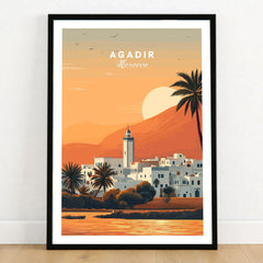 Agadir Travel Poster – Moroccan Mosque and Desert Sunset Art in a black wooden frame leaning against a white wall on a light wooden floor