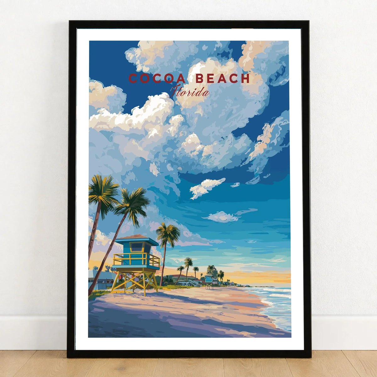 Cocoa Beach Lifeguard Tower Poster - Palm Tree Beach Wall Art in a black wooden frame leaning against a white wall on a light wooden floor