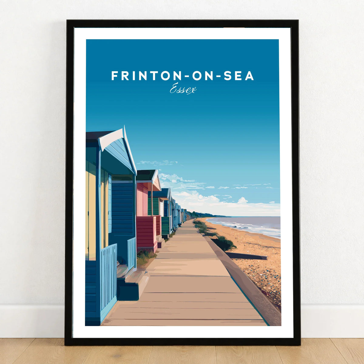 Frinton-on-Sea Travel Poster – Essex Coastline Beach Huts & Prom Art in a black wooden frame leaning against a white wall on a light wooden floor