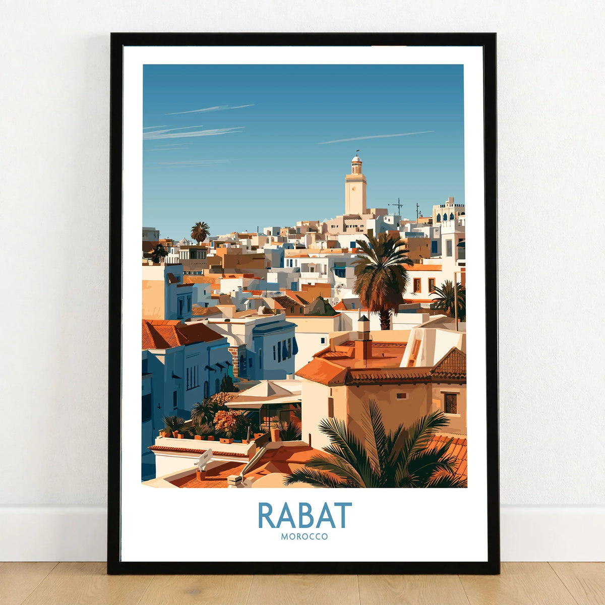Rabat Morocco Minaret Skyline Wall Art — medina rooftops and a pale minaret in late afternoon sun, shown as art print in black frame on wooden floor