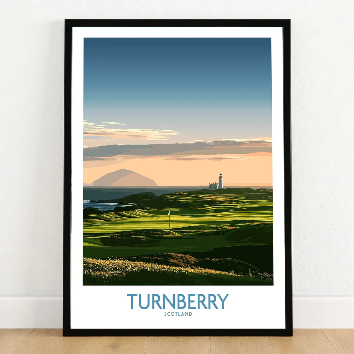 Turnberry Scotland Ayrshire Dusk Wall Art — Ailsa Craig and the white lighthouse across rolling coastal turf at dusk, shown as art print in black frame on wooden floor