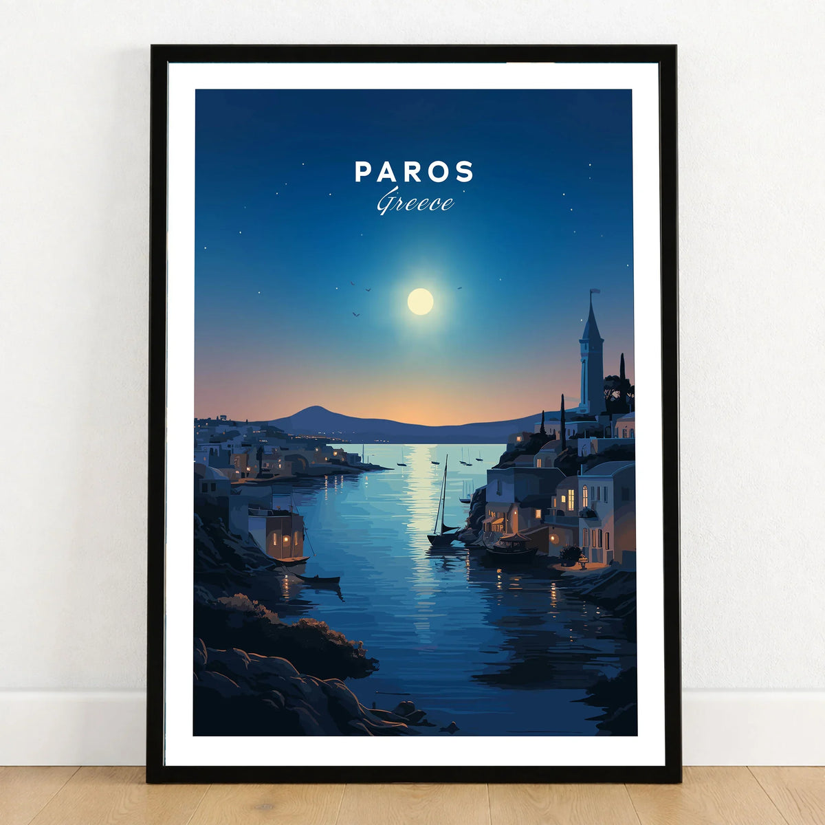 Paros Greece Print in a black wooden frame leaning against a white wall on a light wooden floor