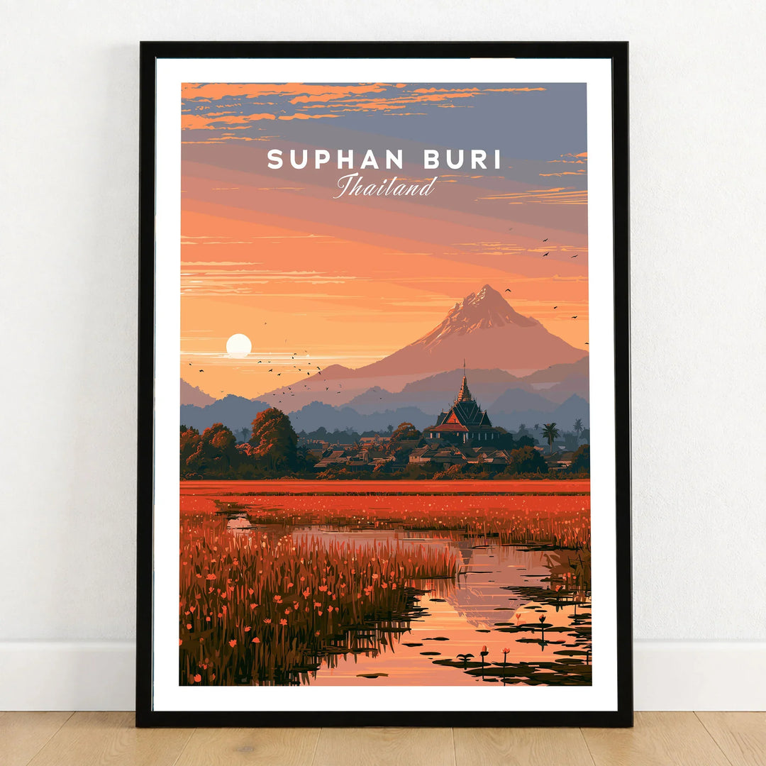 Suphan Buri Thailand Lotus Lake Travel Poster — a lotus-covered lake and temple spire at sunset beneath a mountain peak, shown as art print in black frame on wooden floor