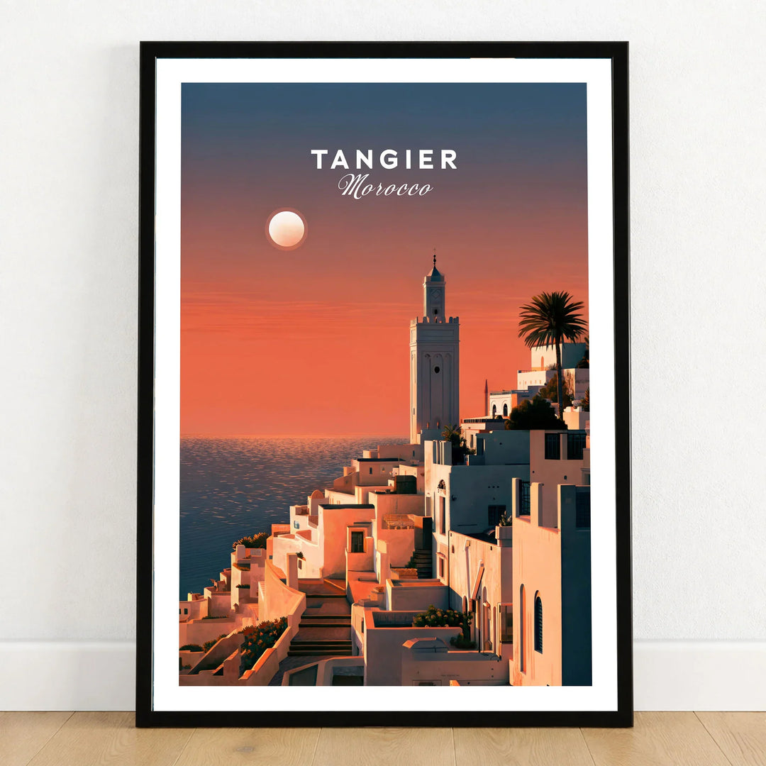Tangier Morocco Golden Hour Travel Poster — a whitewashed hillside town and minaret glowing above the sea at sunset, shown as art print in black frame on wooden floor