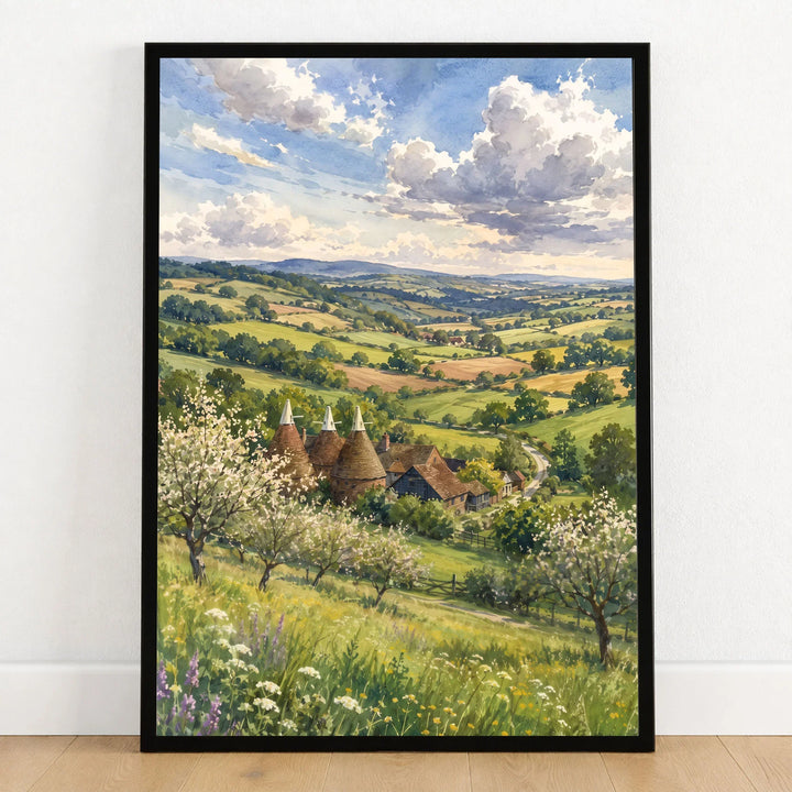 High Weald oast houses and orchard blossom watercolour art print in a black frame on a wooden floor