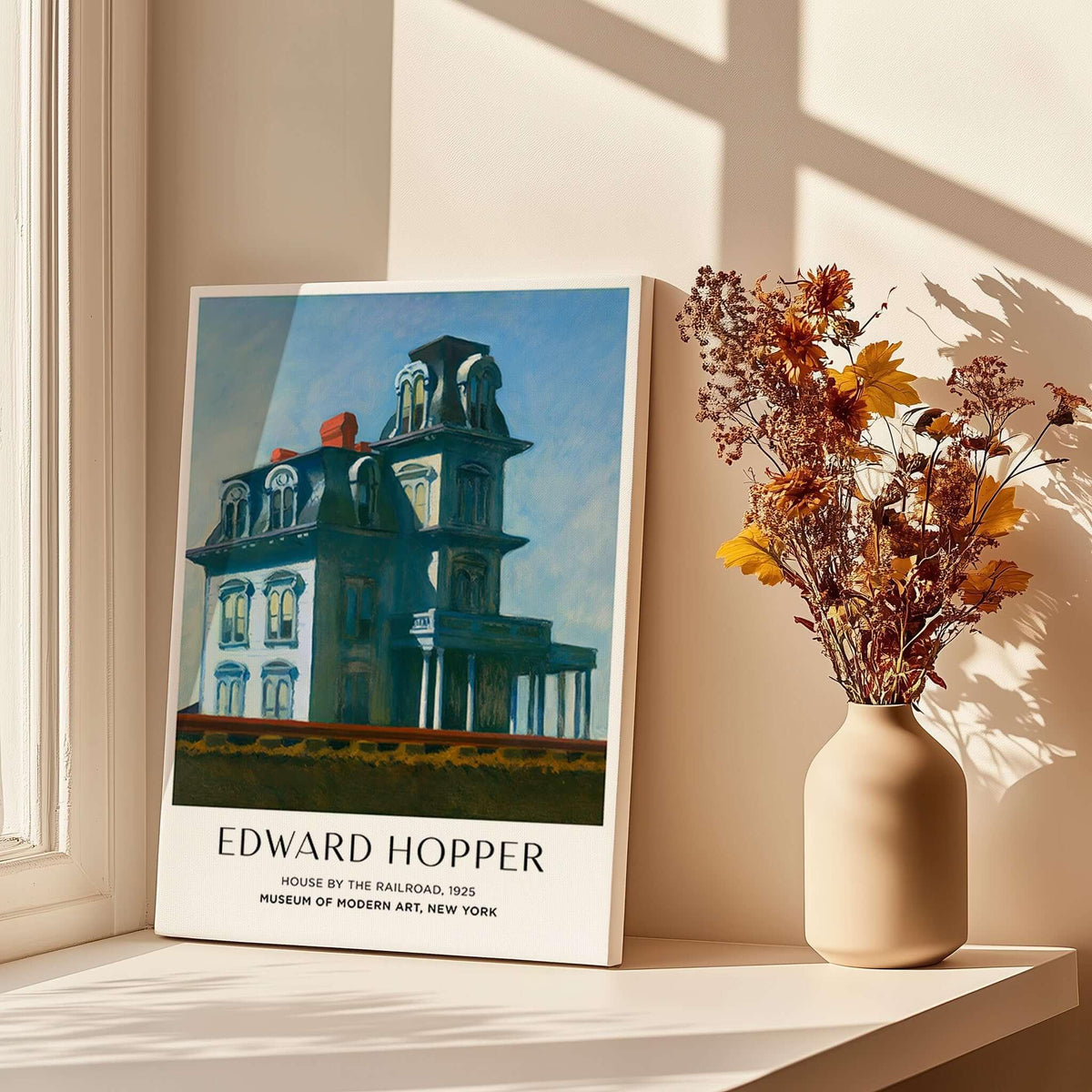 Edward Hopper House by the Railroad 1925 MoMA Art Print Poster displayed beside a vase of flowers in sunlight.