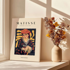 Matisse Art Prints -  Woman in Patterned Hat & Dress Poster displayed on a table with flowers in a vase.