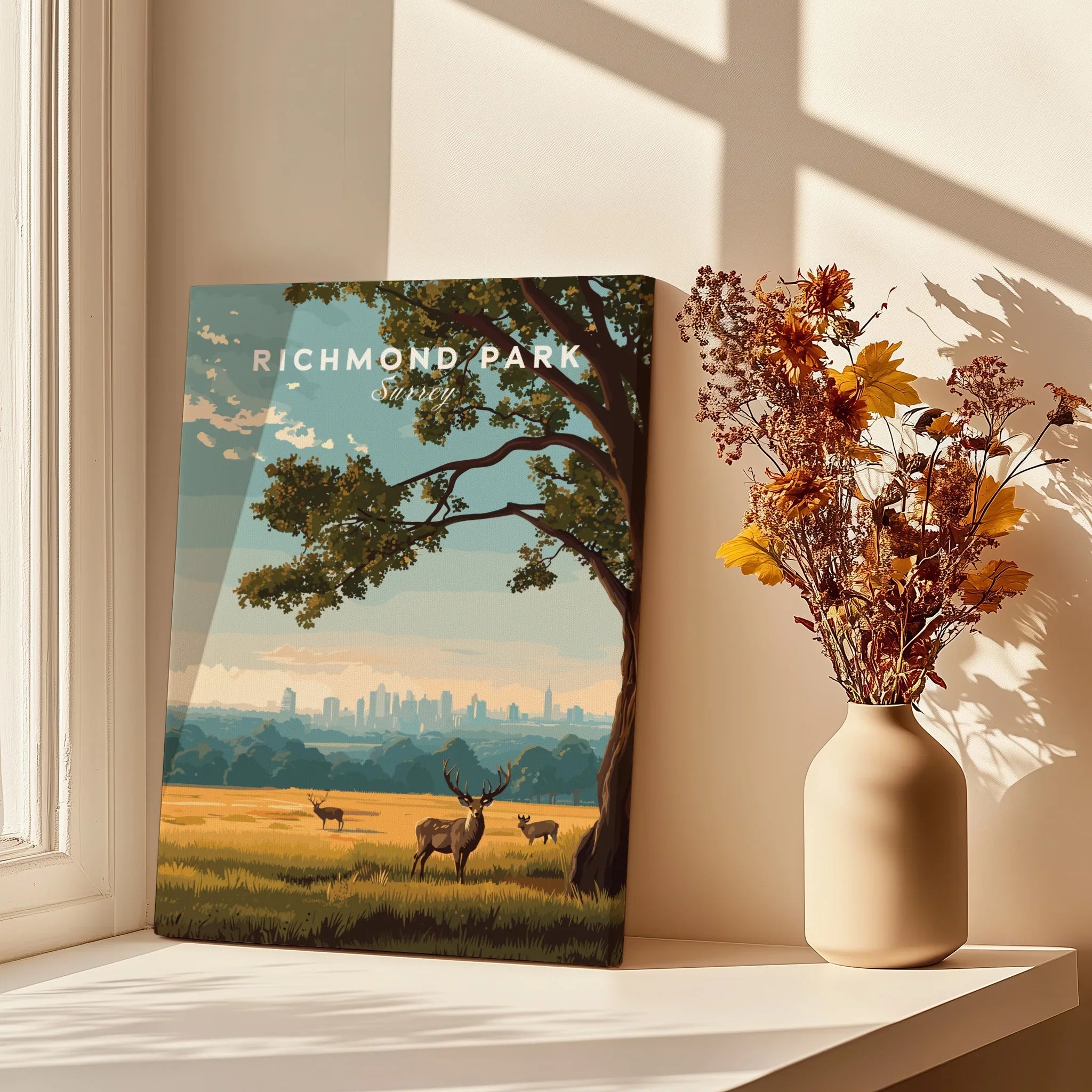 Richmond Park travel poster print with deer and skyline, displayed on sunlit windowsill beside vase of dried flowers