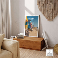 Southwold Print England displayed on wooden table, showcasing colorful beach huts and serene coastal atmosphere.