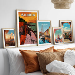 Set of framed travel posters above bed, featuring Acadia National Park and famous city skylines