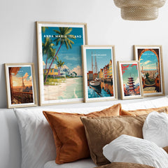 Five framed travel posters above a bed featuring Paris, Anna Maria Island, Copenhagen, Tokyo, and Barcelona.