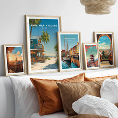 Travel poster wall art set in natural wood frames above bed, featuring Paris, Anna Maria Island, Copenhagen, Tokyo, and Barcelona prints