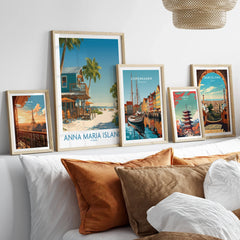 Framed travel posters of Paris, Anna Maria Island, Copenhagen, Tokyo, and Barcelona above a bed.