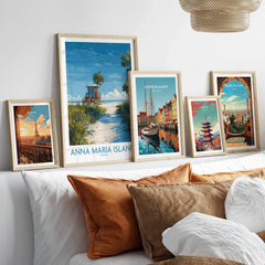 Five travel art prints in natural wood frames above a bed, featuring Paris, Anna Maria Island, Copenhagen, Tokyo, and Barcelona skyline illustrations for modern home decor.