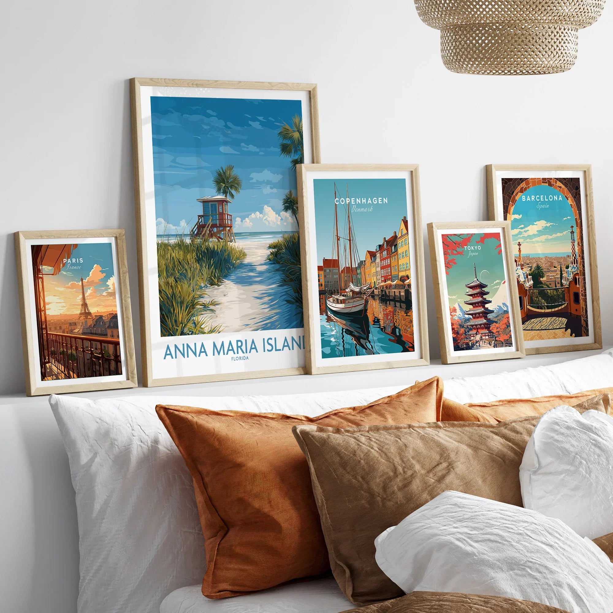 Five travel art prints in natural wood frames above a bed, featuring Paris, Anna Maria Island, Copenhagen, Tokyo, and Barcelona skyline illustrations for modern home decor.