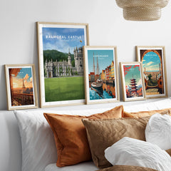 Set of five travel art prints in natural wood frames above a bed, featuring city and landmark illustrations.