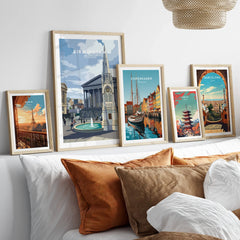 Five framed travel posters of world cities and landmarks above a modern bed with brown pillows.