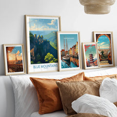 Set of five framed travel art prints featuring Blue Mountains, Paris, Copenhagen, Tokyo, and Barcelona above a bed with neutral pillows.