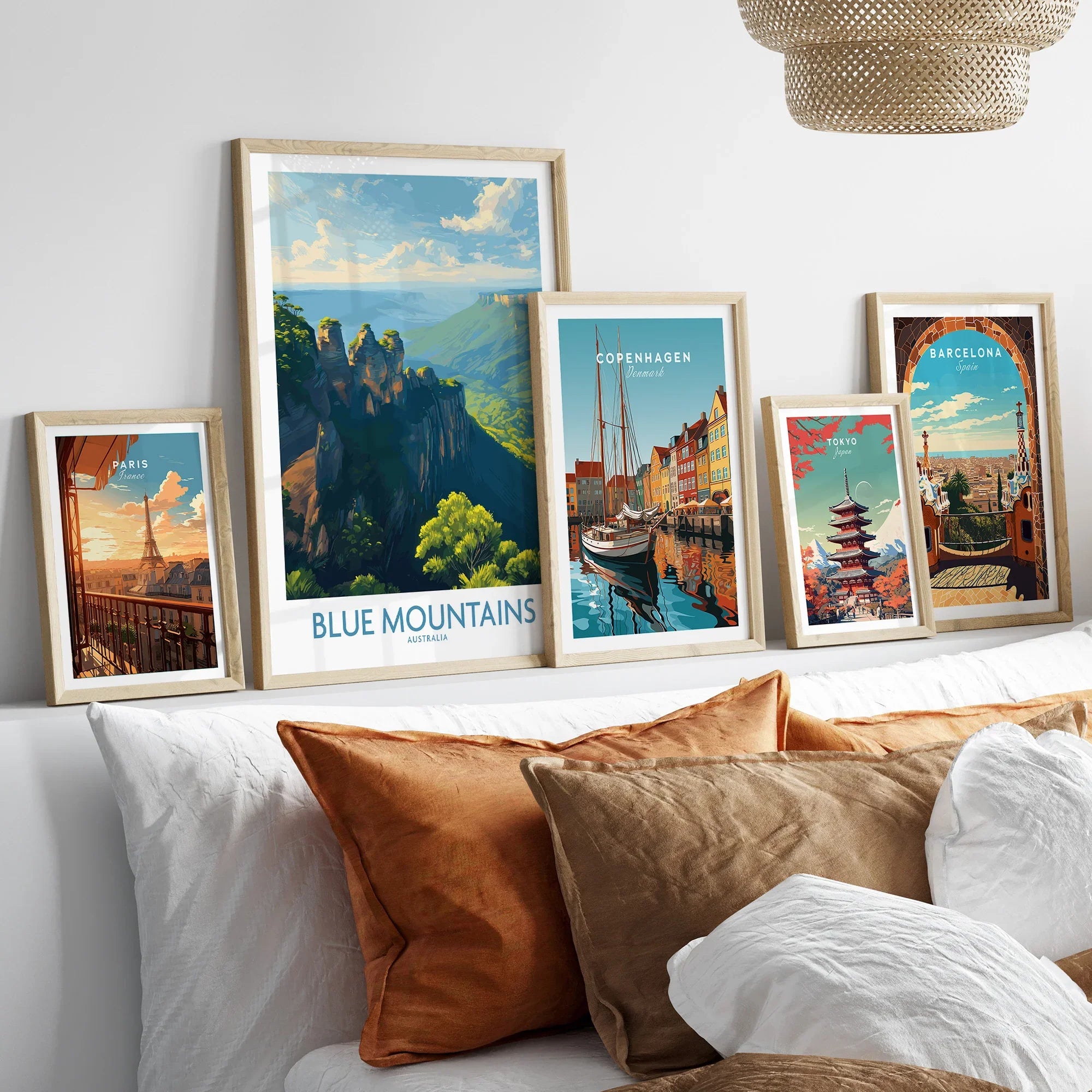 Set of five framed travel art prints featuring Blue Mountains, Paris, Copenhagen, Tokyo, and Barcelona above a bed with neutral pillows.