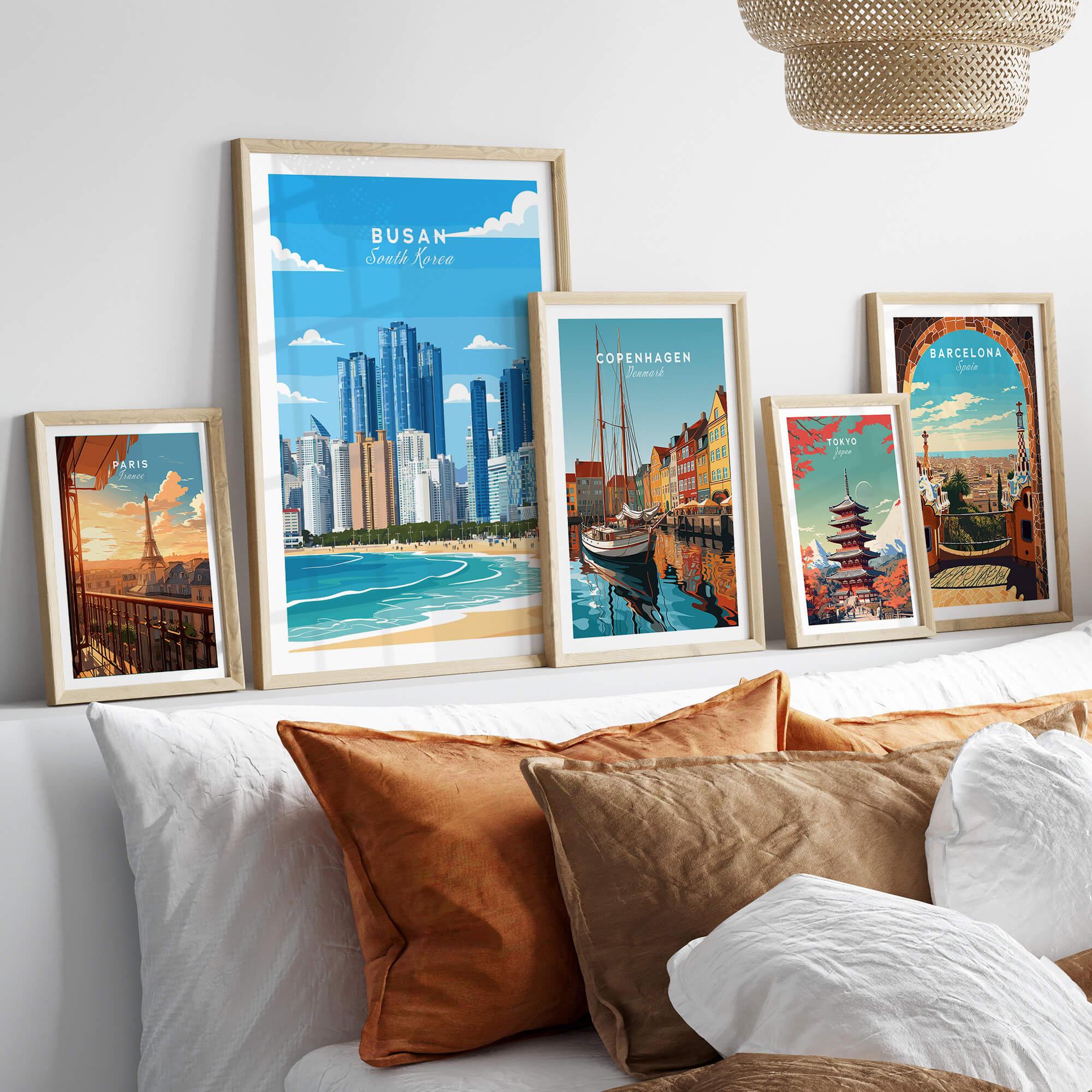 Set of five framed travel posters of world cities above a bed with neutral pillows.