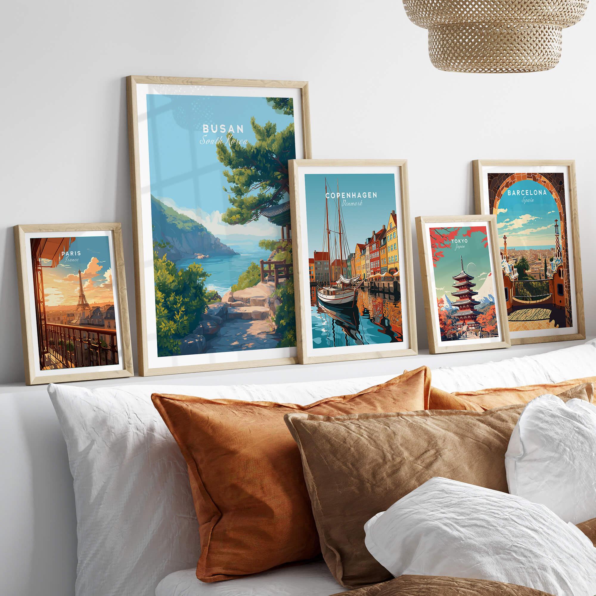 Five framed travel posters featuring Paris, Busan, Copenhagen, Tokyo, and Barcelona above a bed
