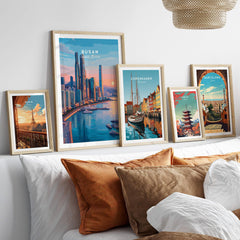 Five framed travel art prints of Paris, Busan, Copenhagen, Tokyo, and Barcelona above a bed