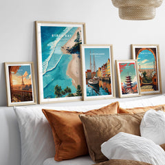 Byron Bay Art Print displayed among other travel art prints on a stylish sofa, showcasing vibrant coastal landscapes.