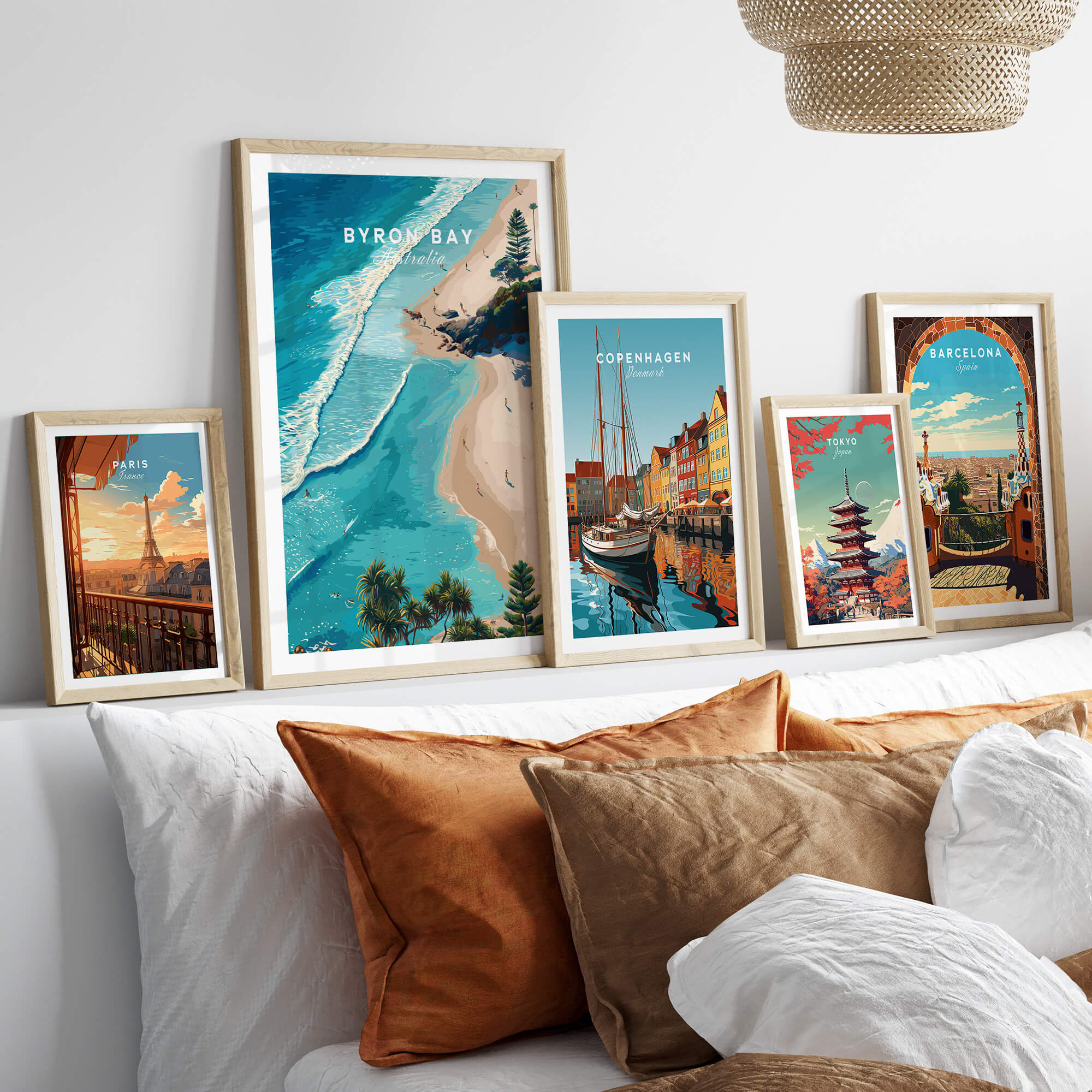 Byron Bay Art Print displayed among other travel art prints on a stylish sofa, showcasing vibrant coastal landscapes.
