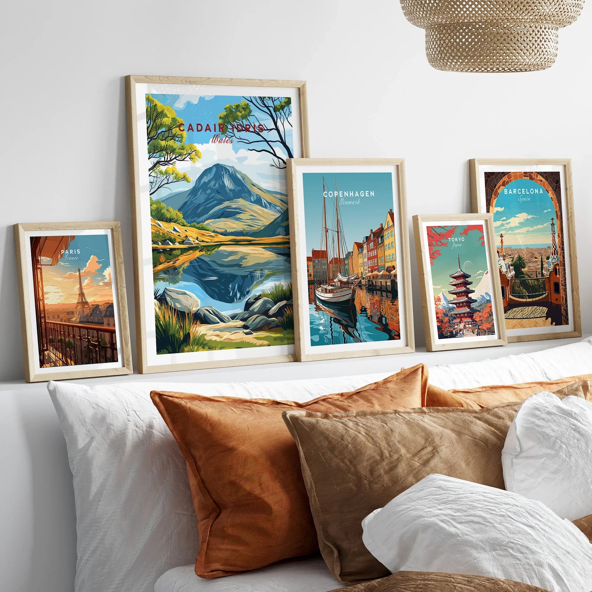 Five framed travel and city posters above a bed, featuring Paris, Copenhagen, Tokyo, Barcelona, and a mountain landscape.