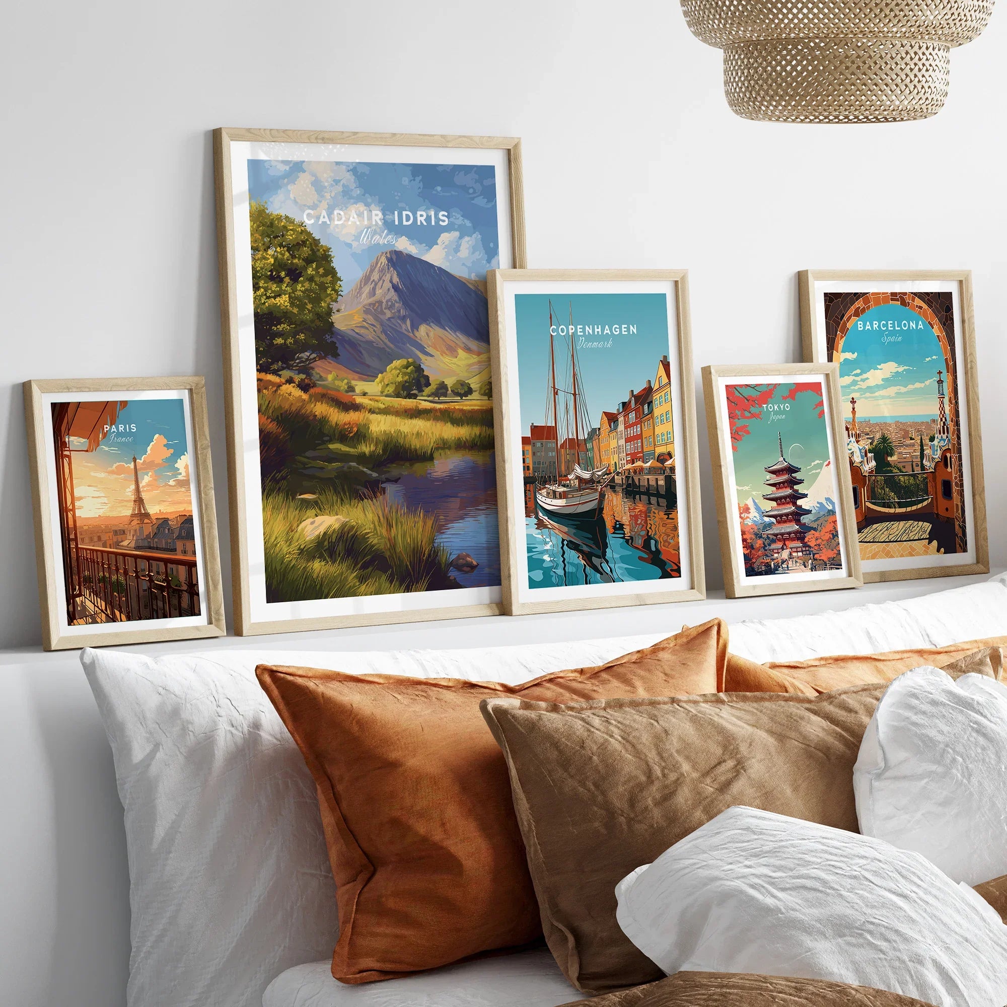 Framed travel art prints above bed featuring landscapes and city skylines including Paris, Tokyo, Copenhagen, Barcelona, and Wales.