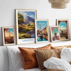 Set of five framed travel posters featuring Paris, Cadair Idris, Copenhagen, Tokyo, and Barcelona above bed with neutral pillows.
