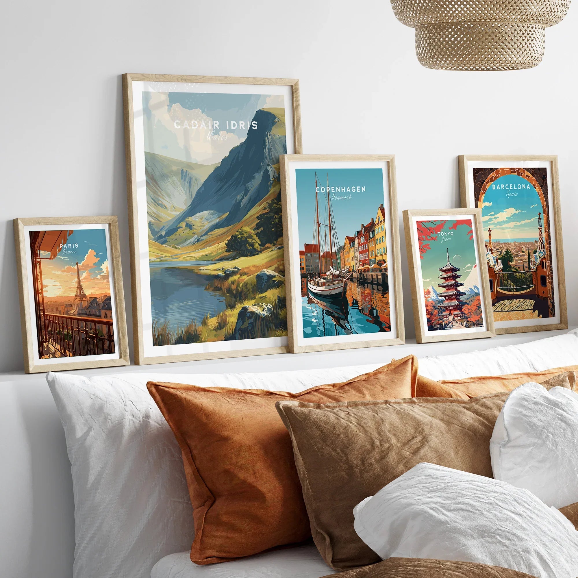 Travel poster art prints in natural wood frames above bed, featuring Paris, Copenhagen, Barcelona, Tokyo, and a scenic mountain landscape.